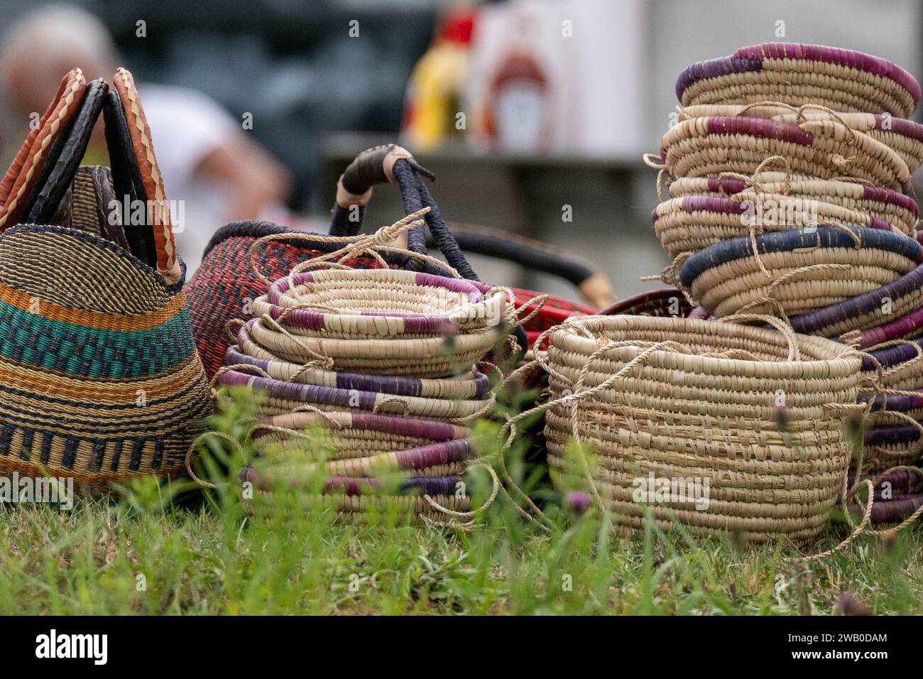 Pile multiple di diversi cestini intrecciati a mano in paglia con bordi colorati. I contenitori fatti in casa sono in vendita presso un mercato agricolo. Foto Stock