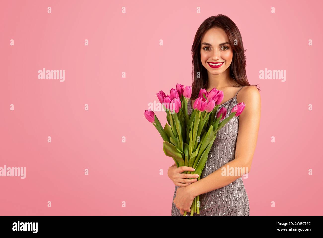 Giovane donna radiosa con un sorriso accattivante, con un bouquet lussureggiante di tulipani rosa Foto Stock