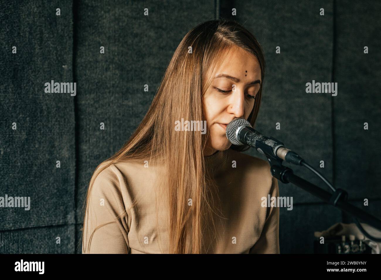 Cantante donna che suona il pianoforte e canta nel microfono, registrando la canzone in uno studio di registrazione audio. Foto Stock