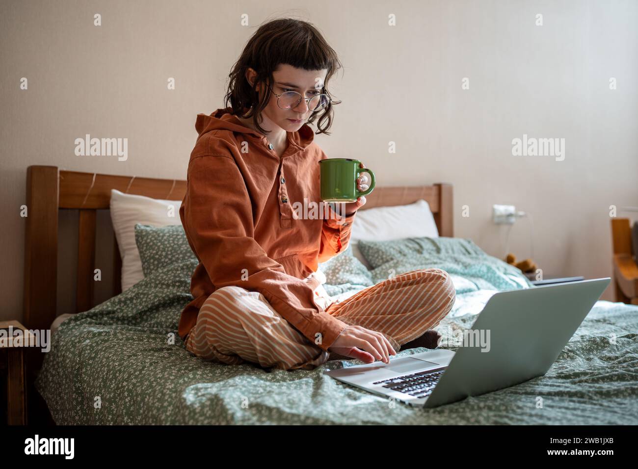 Intelligente diligente ragazza adolescente concentrata seduta a letto, che studia a casa utilizzando un computer portatile Foto Stock