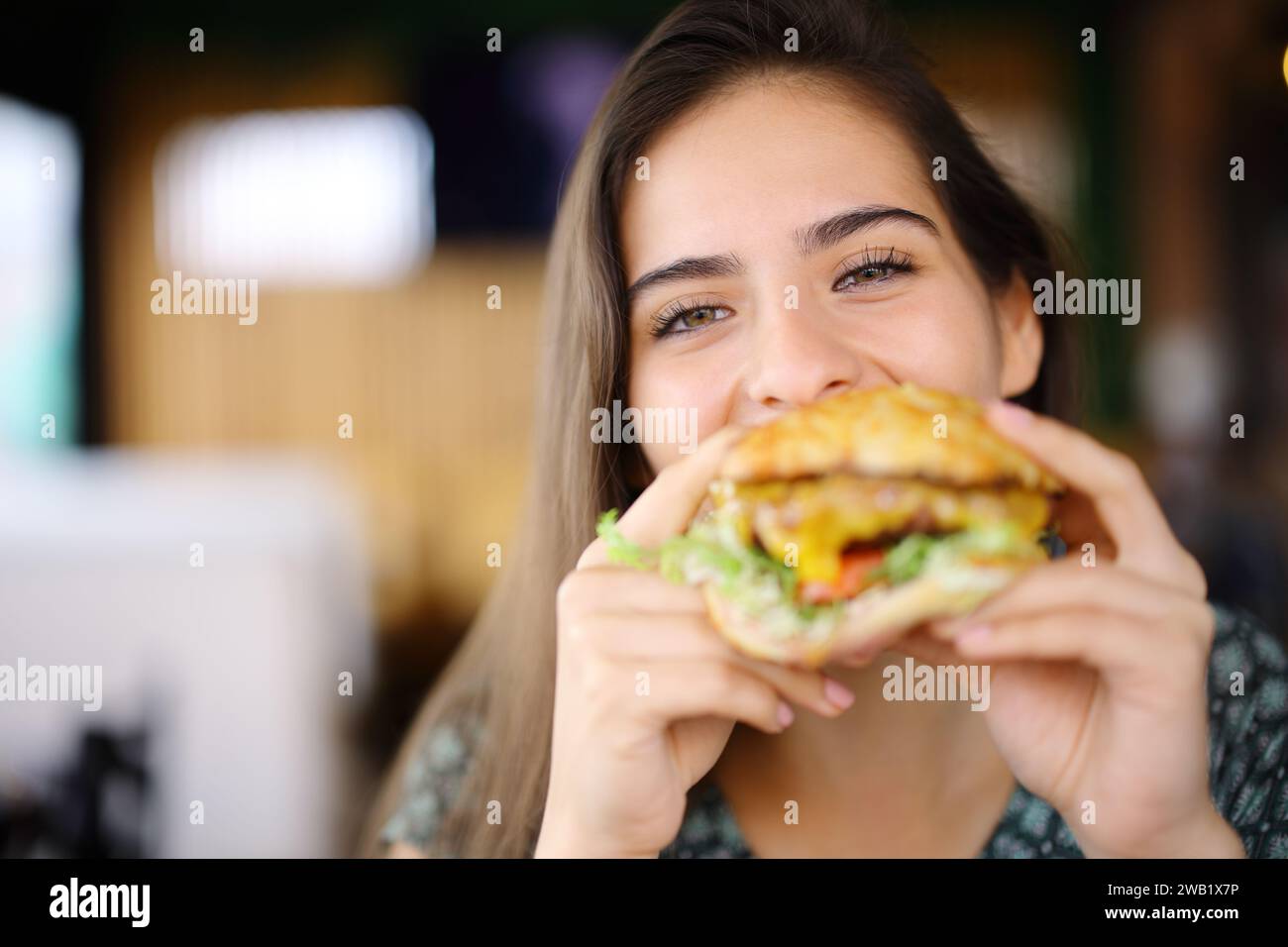 Donna felice che mangia hamburger che ti guarda in un ristorante Foto Stock