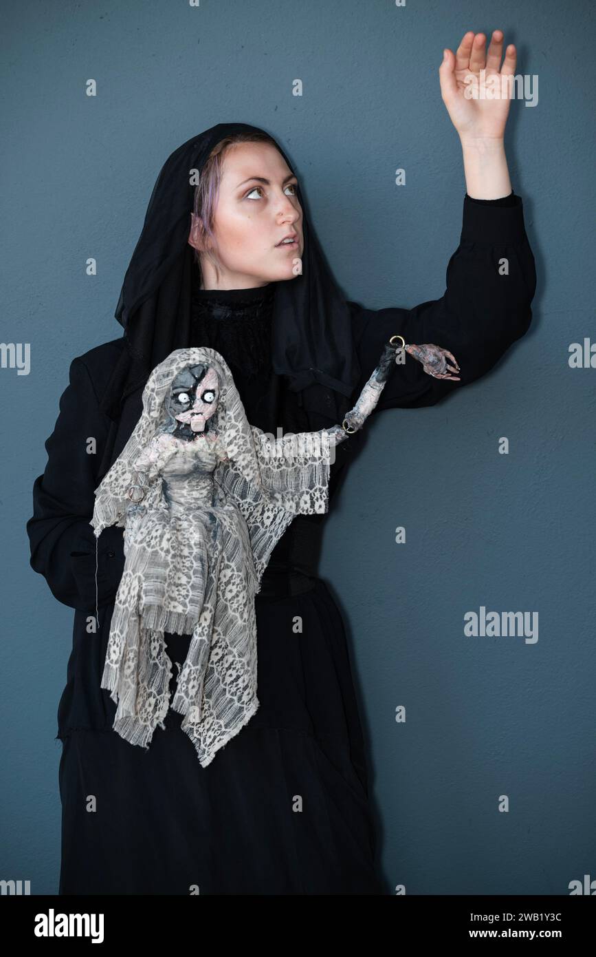 Una cosplayer femminile in costume da strega con una bambola malvagia Foto Stock