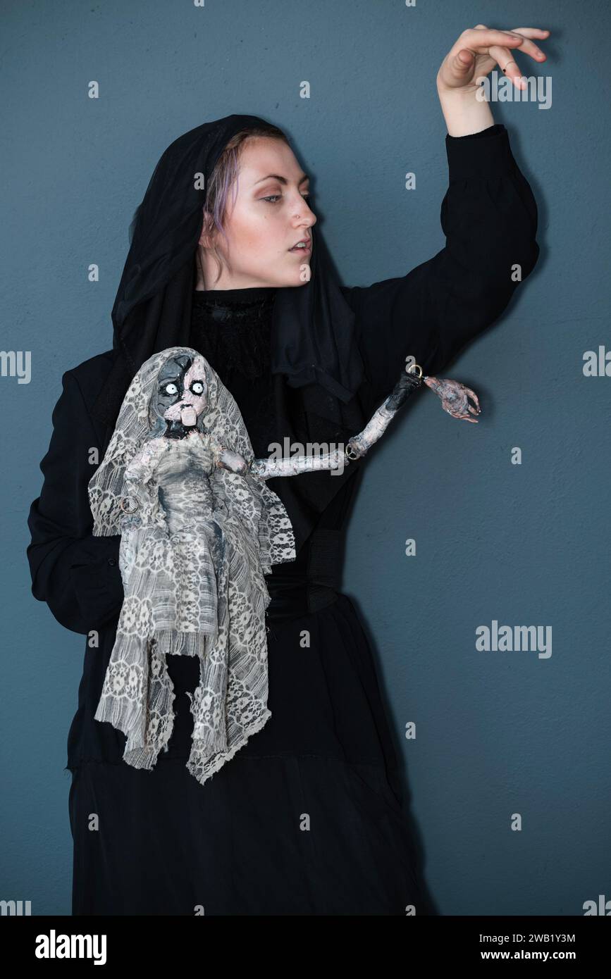 Una cosplayer femminile in costume da strega con una bambola malvagia Foto Stock