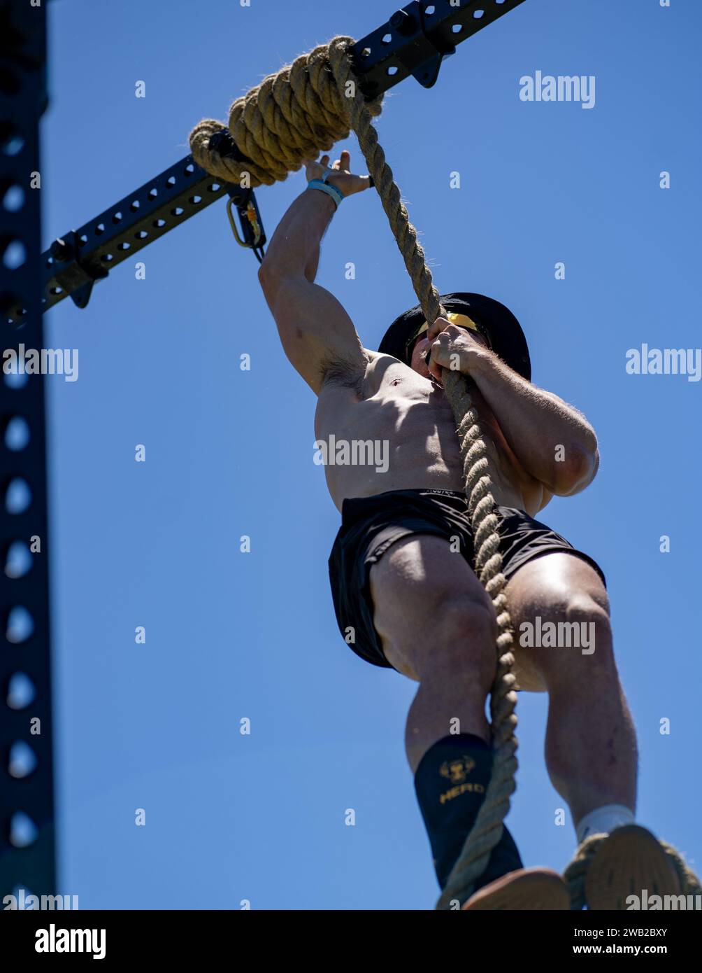 Un uomo atletico sospeso da un'asta verticale, che raggiunge l'alto con una concentrazione determinata Foto Stock