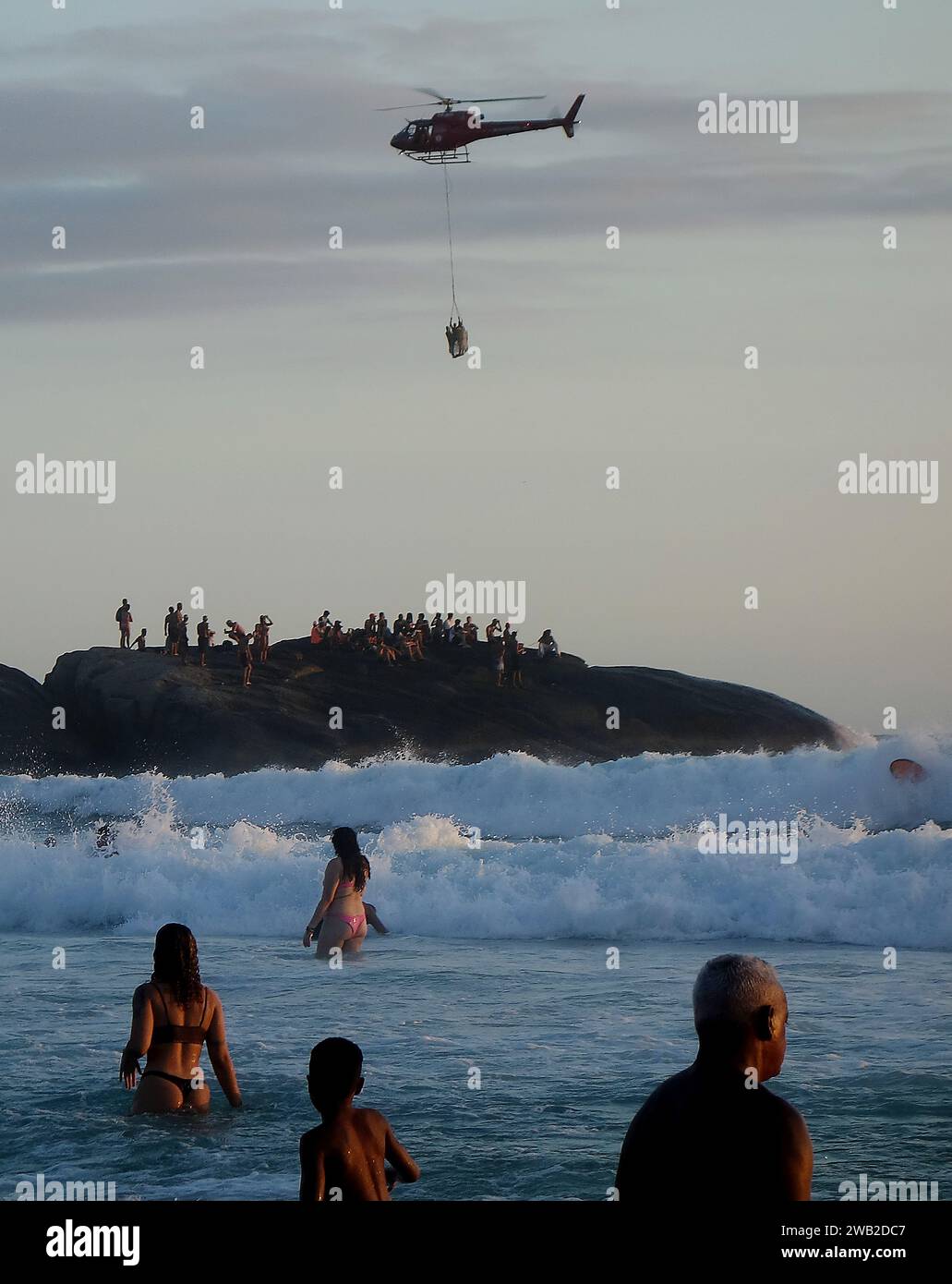 Rio de Janeiro, Rio de Janeiro, Brasile. 7 gennaio 2024. Il Rio de Janeiro Air Sea Rescue ha eseguito con successo un'operazione di salvataggio al tramonto sulla spiaggia di Ipanema, salvando un nuotatore in difficoltà. Sullo sfondo delle pietre di Arpoador, un elicottero ha portato l'individuo salvato davanti a centinaia di persone che si riuniscono ogni giorno per assistere agli splendidi tramonti. Questo incidente ha sottolineato l'intensa attività nelle acque di Rio dall'inizio del nuovo anno, con un notevole aumento delle operazioni di salvataggio che rispondono alle condizioni di surf. (Immagine di credito: © Bob Karp/ZUMA Press Wire) SOLO USO EDITORIALE! Foto Stock