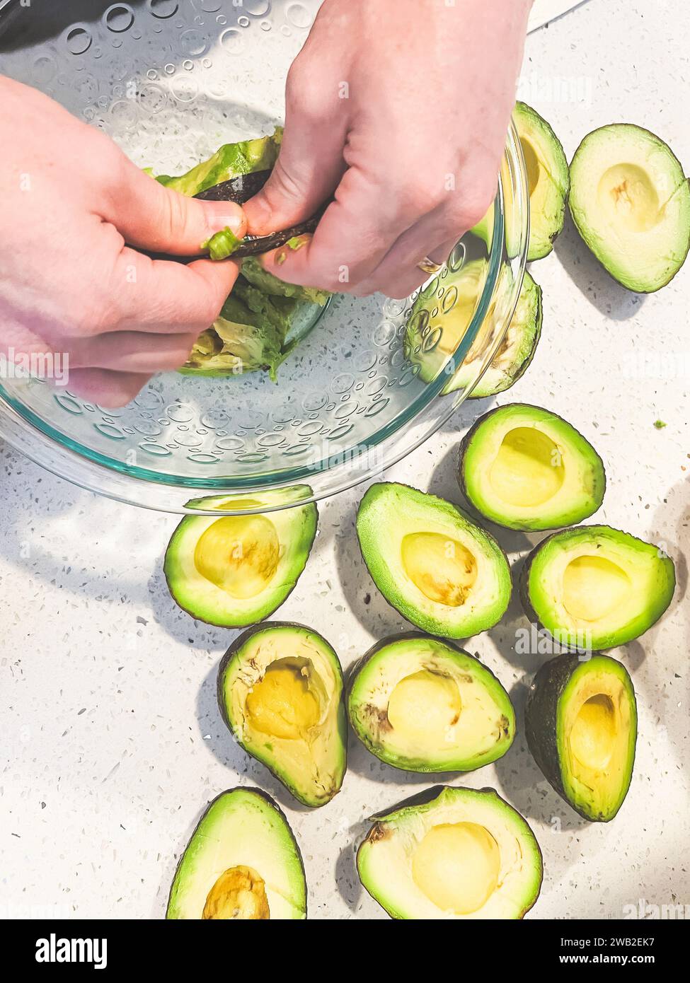 Mani che pescano avocado in una ciotola di vetro Foto Stock