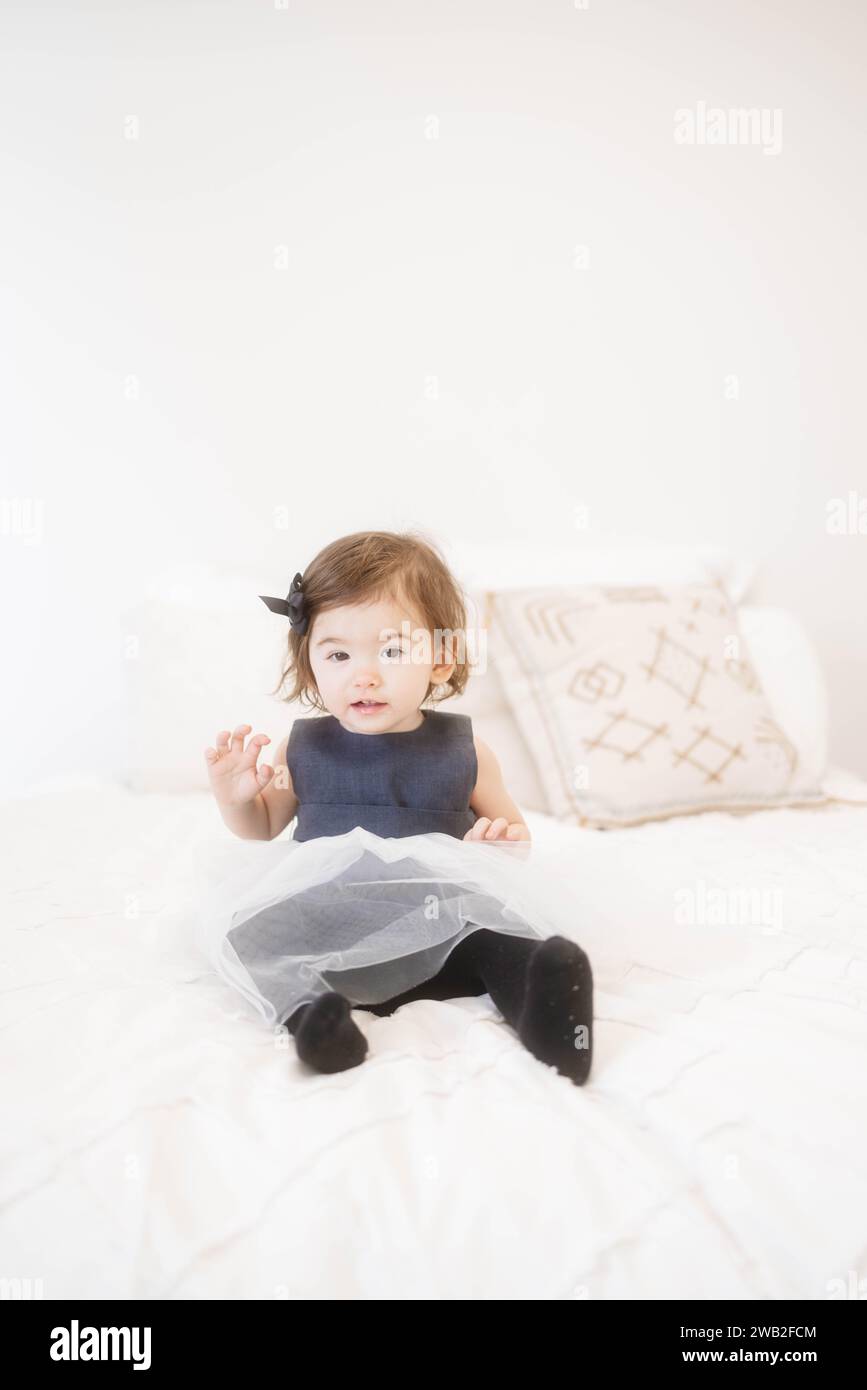 Bambina in abito Tulle Navy seduta su un letto Foto Stock