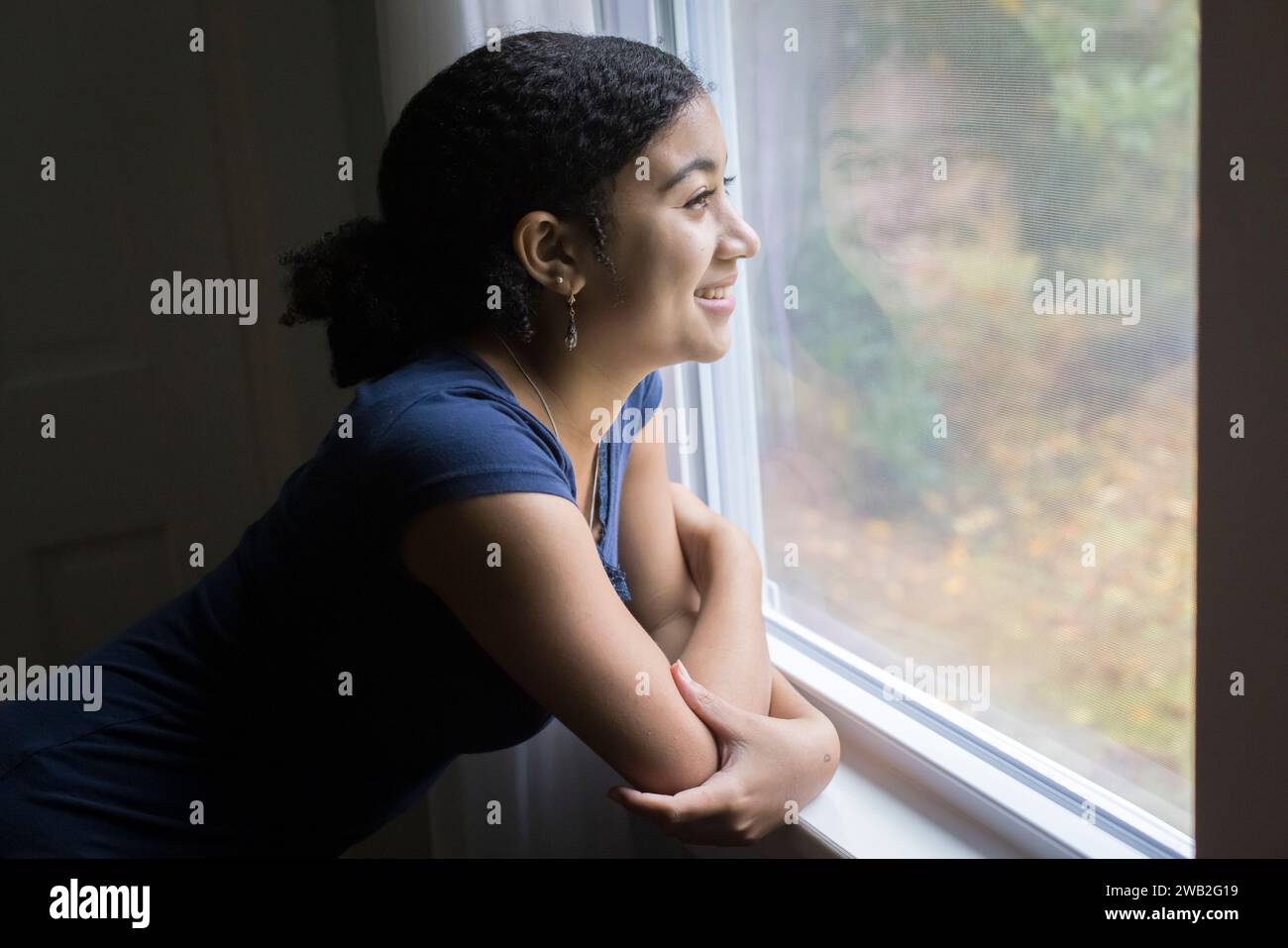 Una ragazzina birazziale sorridente guarda fuori da una finestra Foto Stock