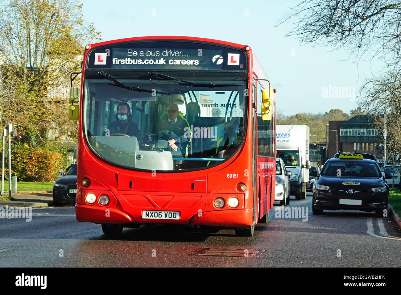 Formazione per essere un autista di autobus supervisionato da un istruttore maschio qualificato, un veicolo commerciale rosso a un piano che guida lungo il traffico Essex Inghilterra Regno Unito Foto Stock