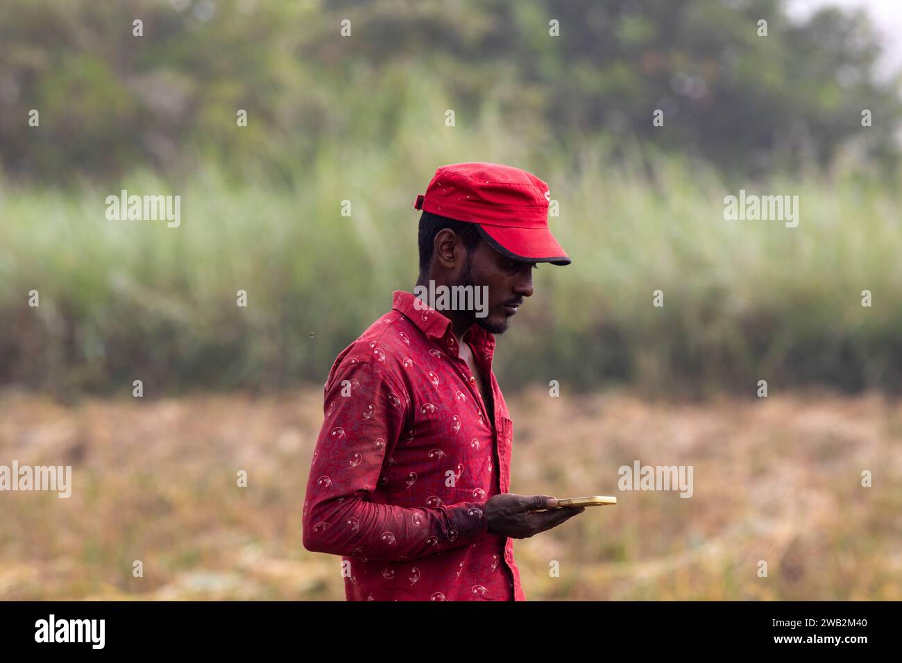 Chattogram, Bangladesh. 17 dicembre 2023. Un contadino sta camminando con uno smartphone in mano vicino a gumai beel sulla rangunia upazila. SOLO PER USO EDITORIALE! Non Fo Foto Stock