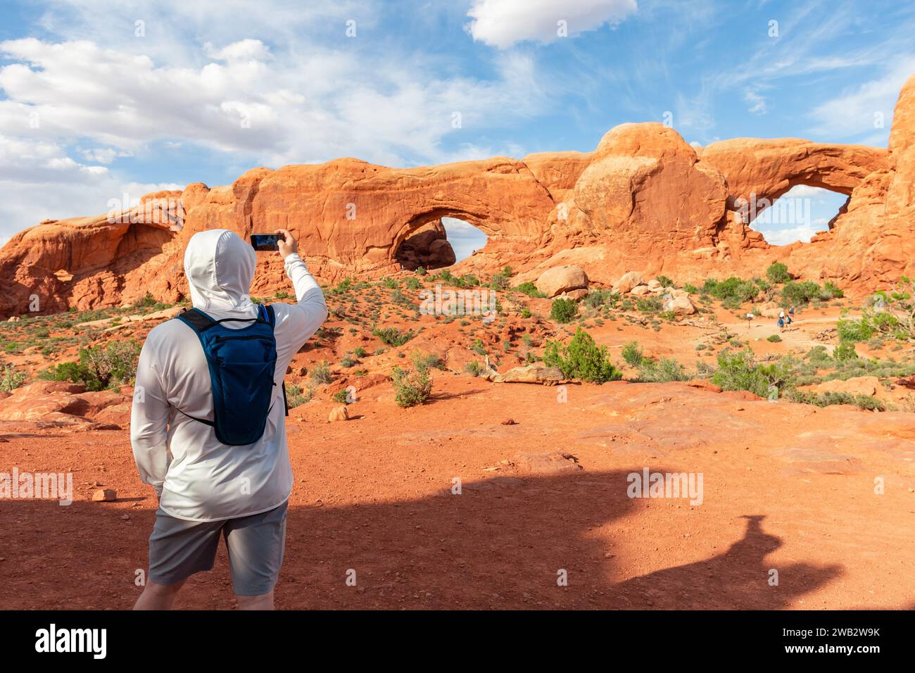 Il turista indossa indumenti protettivi per il sole e zaino in acqua per scattare una foto del South e del North Window Arch nel Parco Nazionale degli Arches nello Utah. Foto Stock