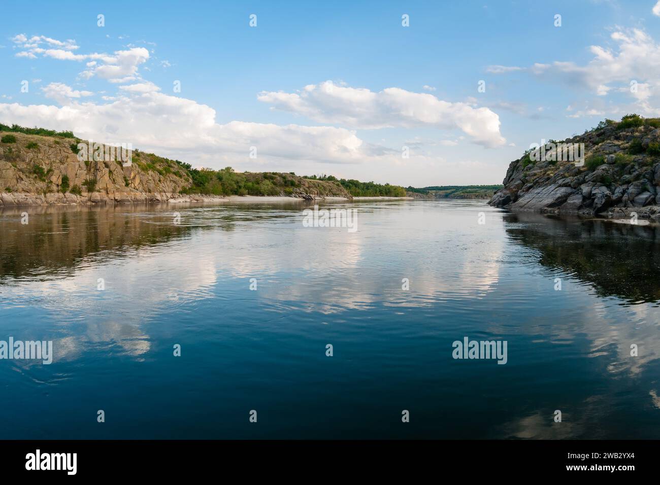 Grandi nuvole di cumulus si riflettono nell'acqua di un ampio fiume con alte sponde rocciose nella foresta e una lunga spiaggia sullo sfondo Foto Stock Grandi nuvole di cumulus si riflettono nell'acqua di un ampio fiume con alte sponde rocciose nella foresta e una lunga spiaggia sullo sfondo Foto Stock