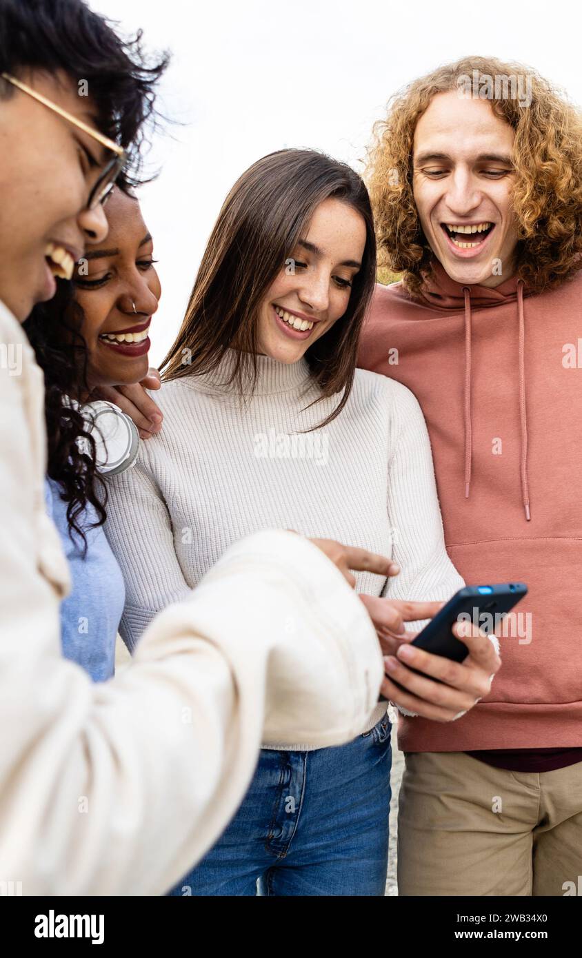 Felici amici diversi che ridono mentre guardano video divertenti sullo smartphone Foto Stock