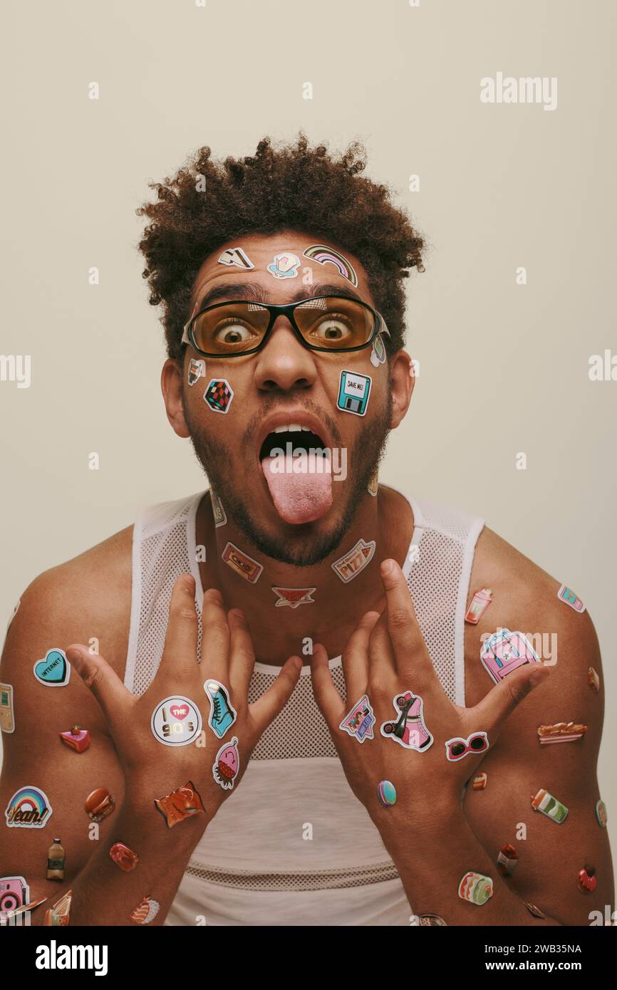eccentrico giovane afro-americano con occhiali da sole con adesivi di tendenza sul viso su sfondo grigio Foto Stock