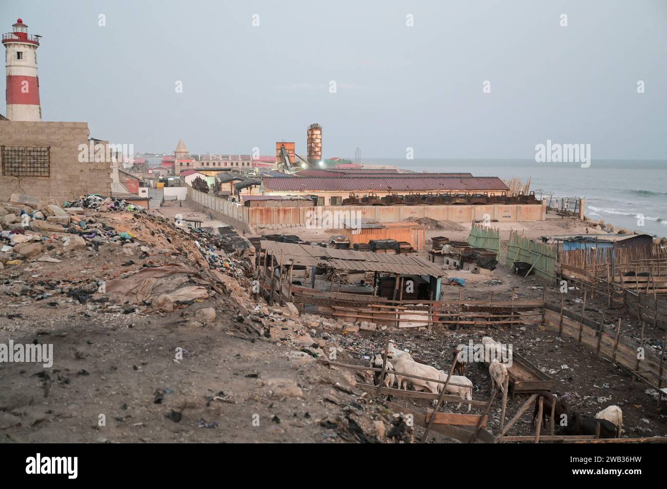 GHANA, Accra, Jamestown, faro dell'epoca coloniale britannica e allevamento di bestiame nell'oceano atlantico, dietro il cantiere del nuovo porto di pesca da parte della società cinese CRCC China Railway Construction Corporation Limited e China Aid / GHANA, Accra, Jamestown Leuchtturm aus der britischen Kolonialzeit, Kuhställe am Strand, hinten Baustelle eines neuen Fischerei Hafen durch chinesische Baufirma CRCC und China Aid Foto Stock