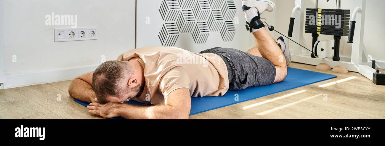 uomo sdraiato a faccia in giù su un tappetino per il fitness e allenarsi su una macchina per esercizi nel centro kinesio, banner Foto Stock
