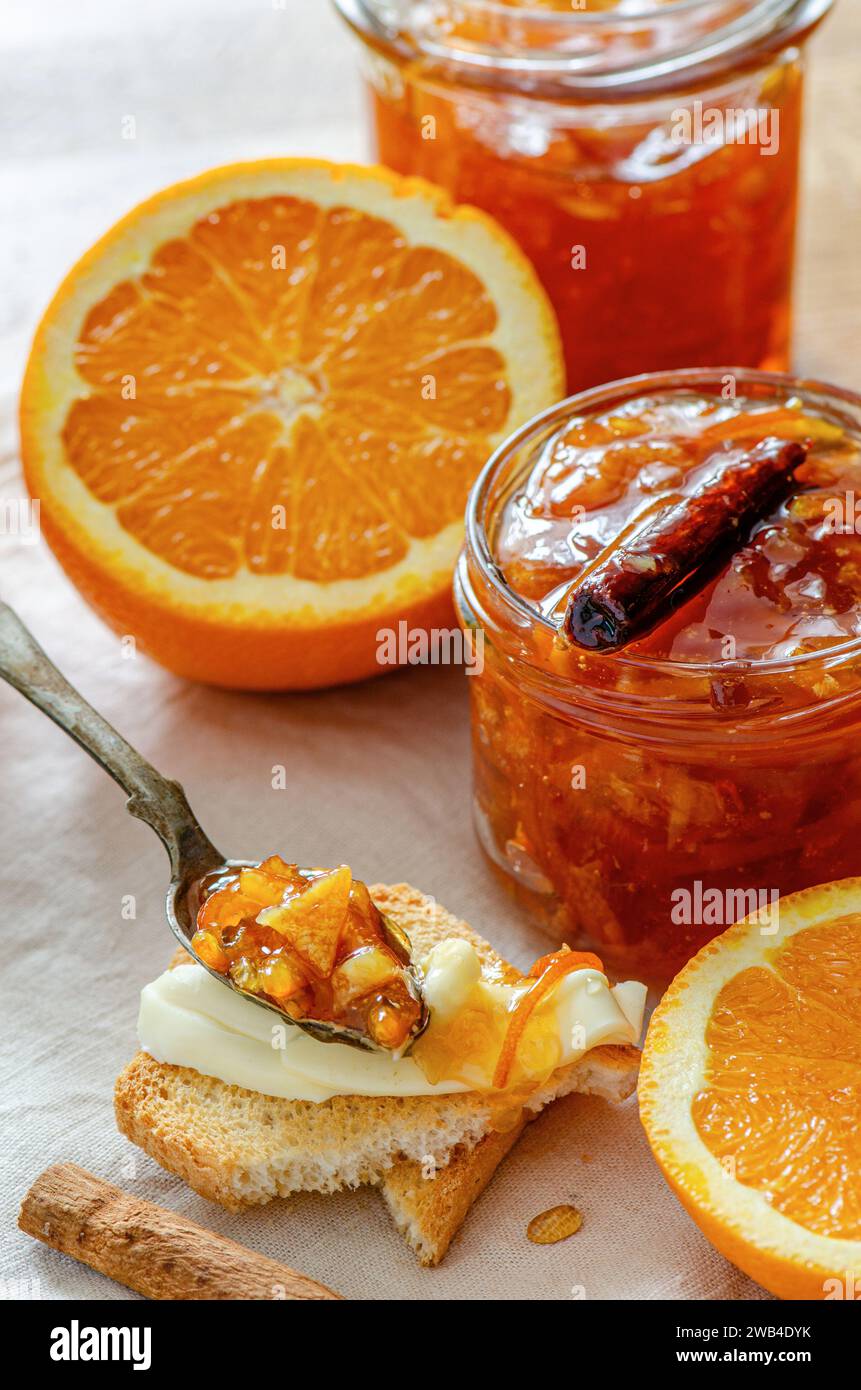 Un barattolo di marmellata d'arancia fatta in casa con frutti d'arancia tagliati, bastoncino di cannella e cucchiaio da tè rustico Foto Stock