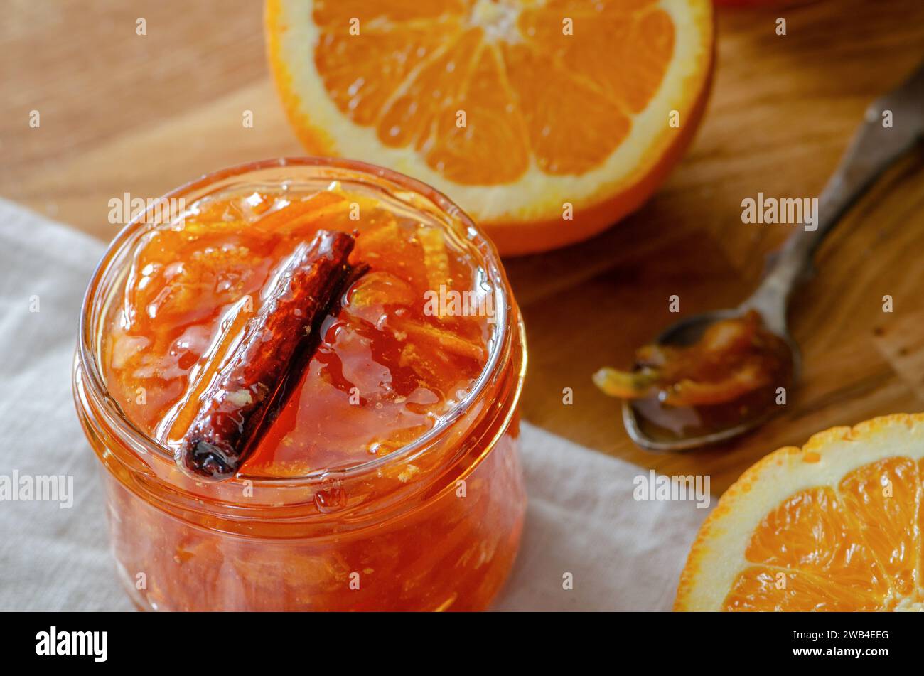 Un barattolo di marmellata d'arancia fatta in casa con frutti d'arancia tagliati, bastoncino di cannella e cucchiaio da tè rustico Foto Stock