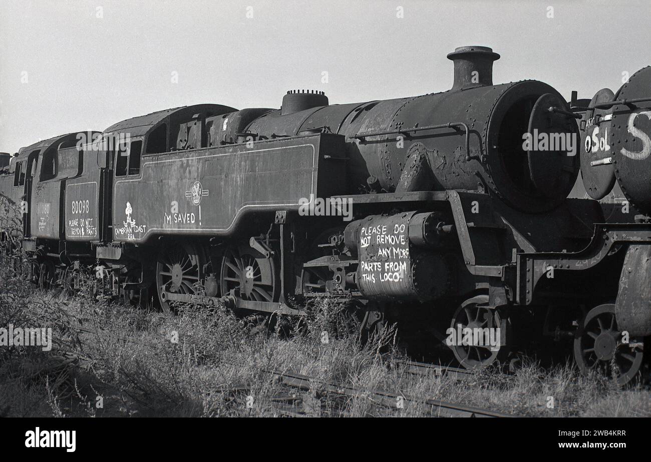 1975, storica, una vecchia locomotiva a vapore, 80098 seduto su un binario ferroviario presso lo scrapyard Woodham Brothers a Barry Docks, Galles del Sud, UK.commonly conosciuto come il Barry Srapyard. Scrivendo sul lato dice, Cambrian Coast RPA sono salvo! Si prega di non rimuovere più parti da questa località....i Woodham Brothers, commercianti di rottami di metallo fondati nel 1892, portarono le vecchie locomotive a vapore della Briitsh Railways, le immagazzinarono e poi le vendettero o le demolirono. Si stima che oltre 200 locomotive a vapore siano state salvate per il movimento di conservazione delle ferrovie. Foto Stock