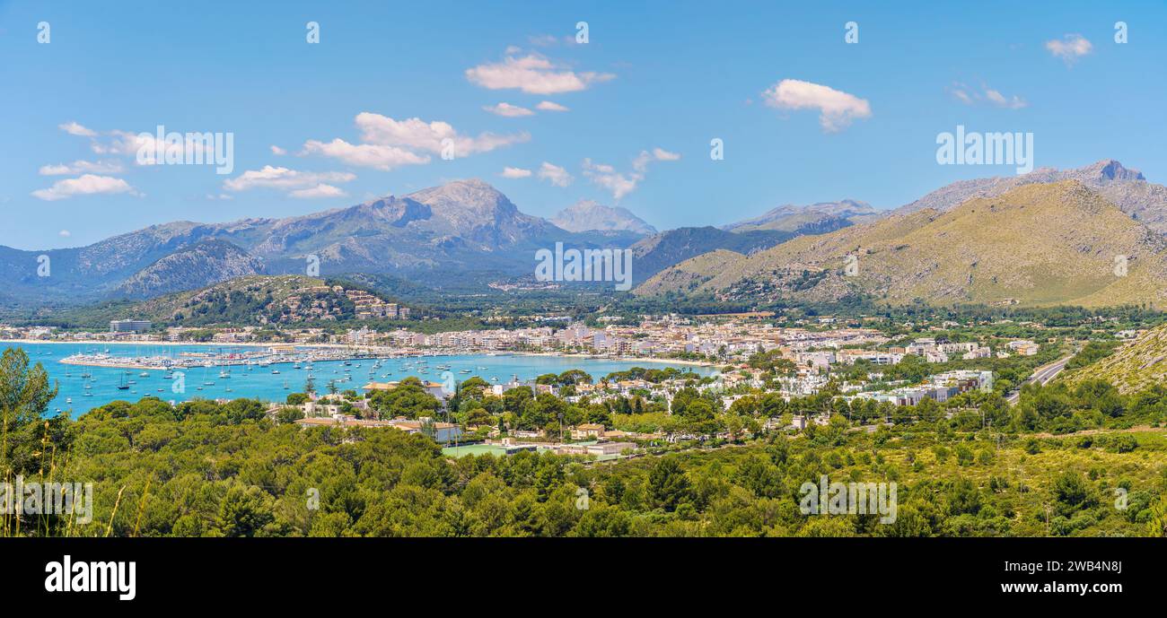 Vista panoramica di Port de Pollena, annidato vicino alla Serra de Tramuntana, con acque azzurre e un vivace porticciolo turistico, un gioiello nella corona di Maiorca. Foto Stock