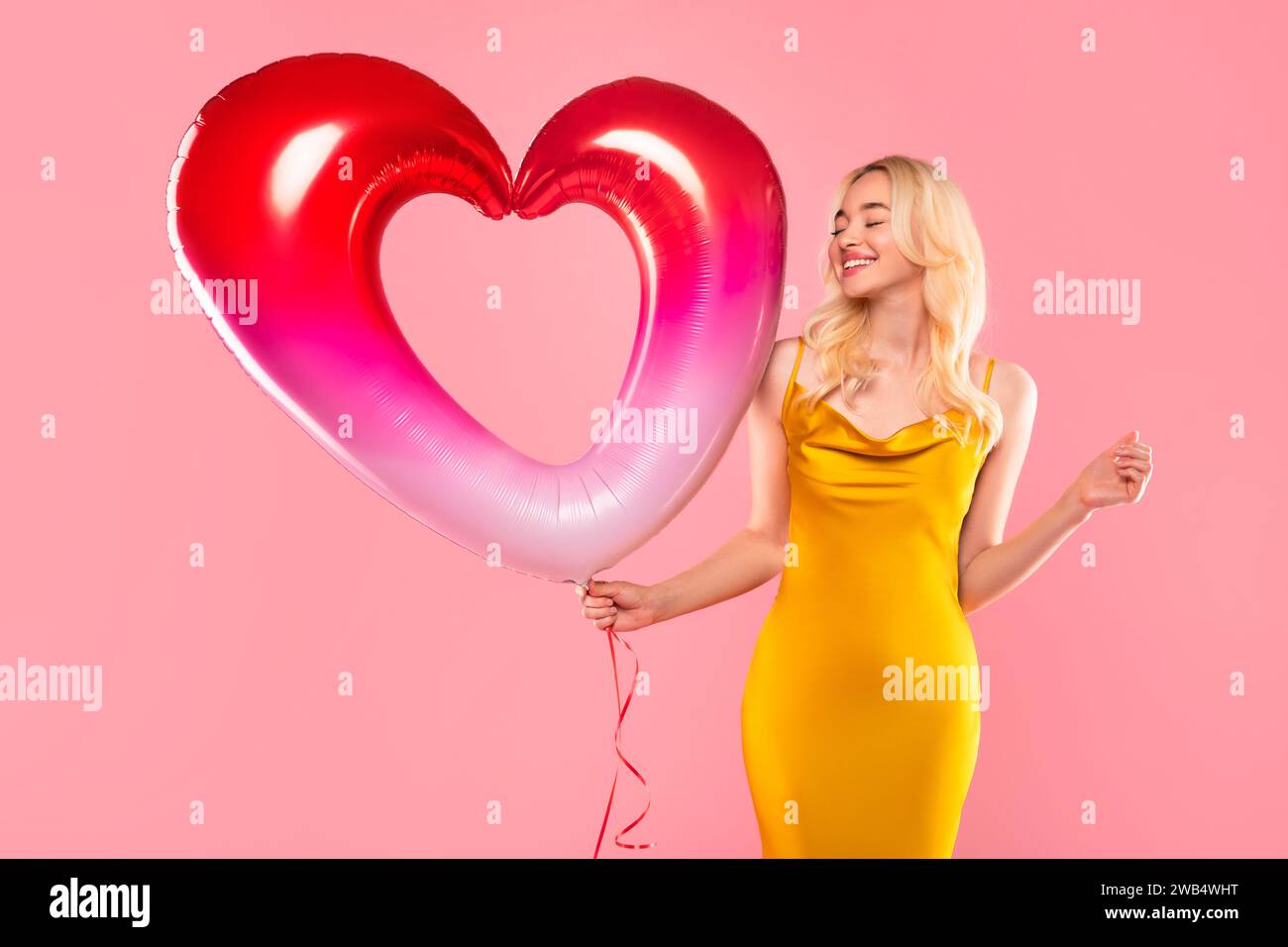 Donna felice con un palloncino dal cuore vivace su sfondo rosa Foto Stock