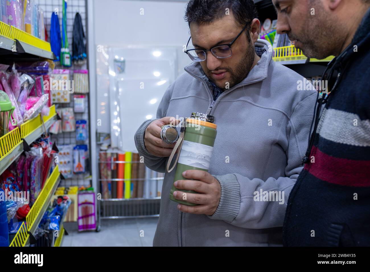 l'uomo controlla la tazza termica in negozio per l'acquisto, controllando le specifiche e la durata dell'isolamento con l'aiuto del proprietario del negozio Foto Stock
