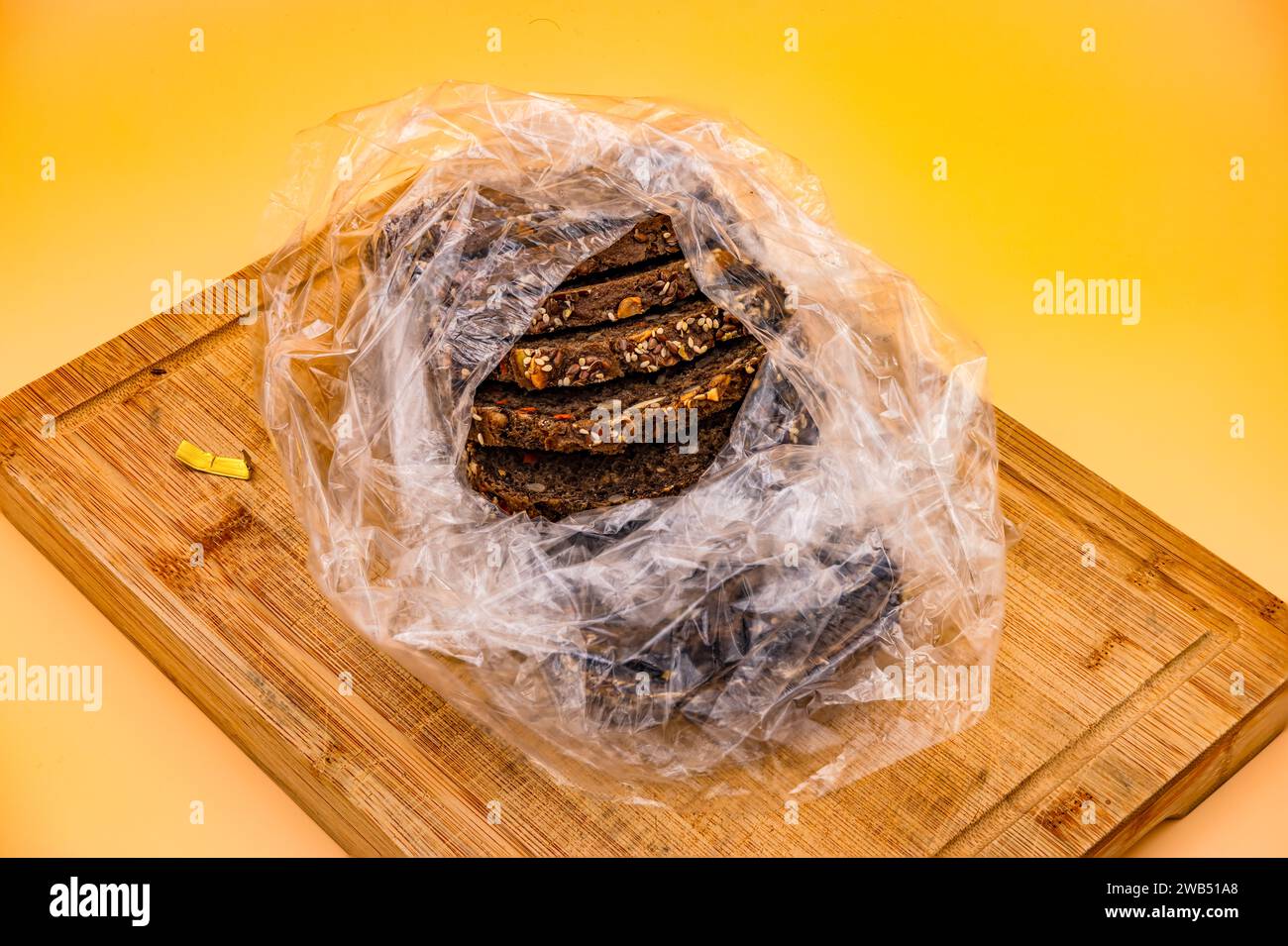 Pane integrale appena sfornato a fette in una busta di plastica fotografata su un tagliere su uno sfondo giallo nello studio Foto Stock