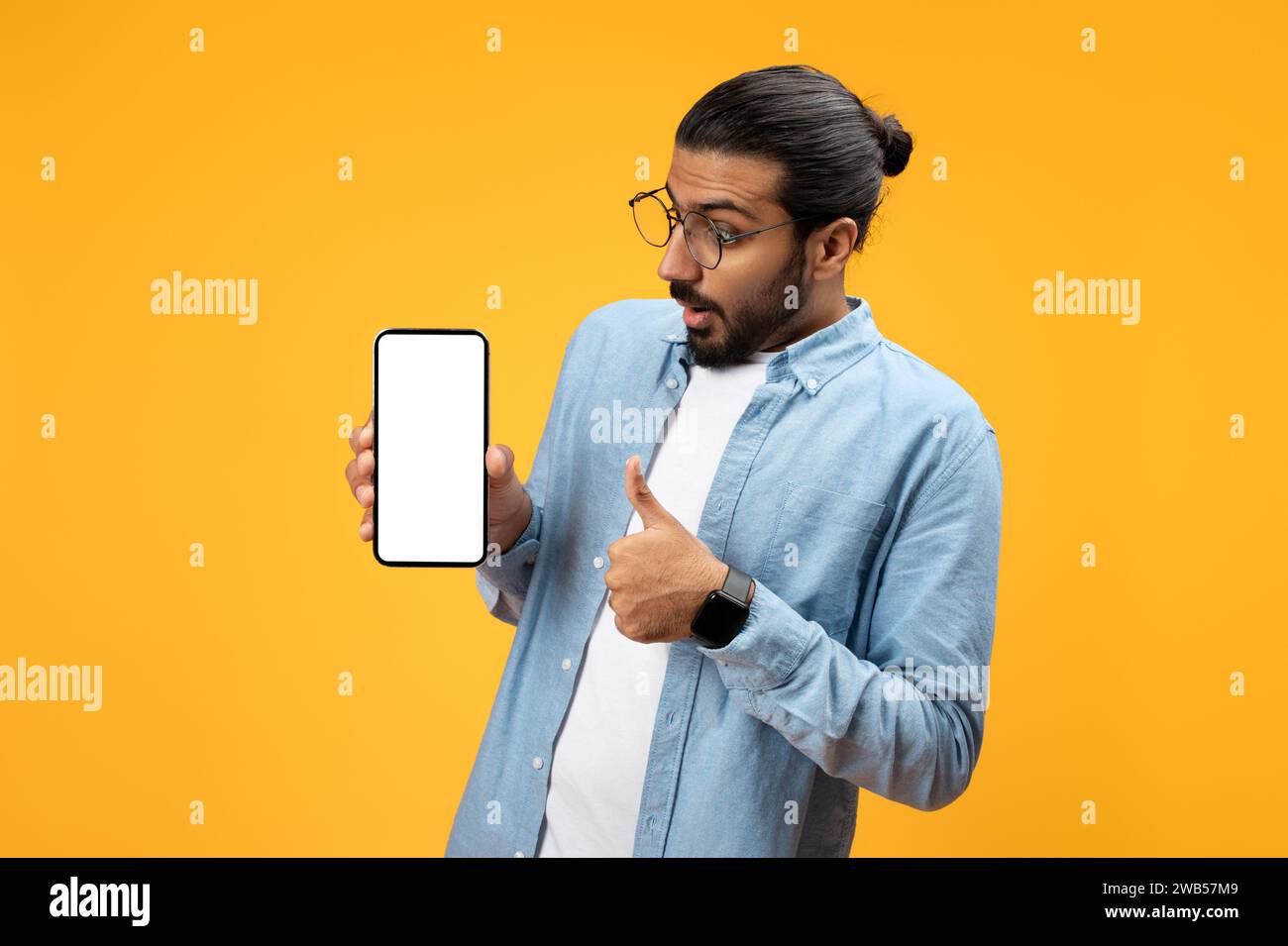 Un uomo sorpreso con una camicia in denim azzurro regge uno smartphone con uno schermo vuoto Foto Stock