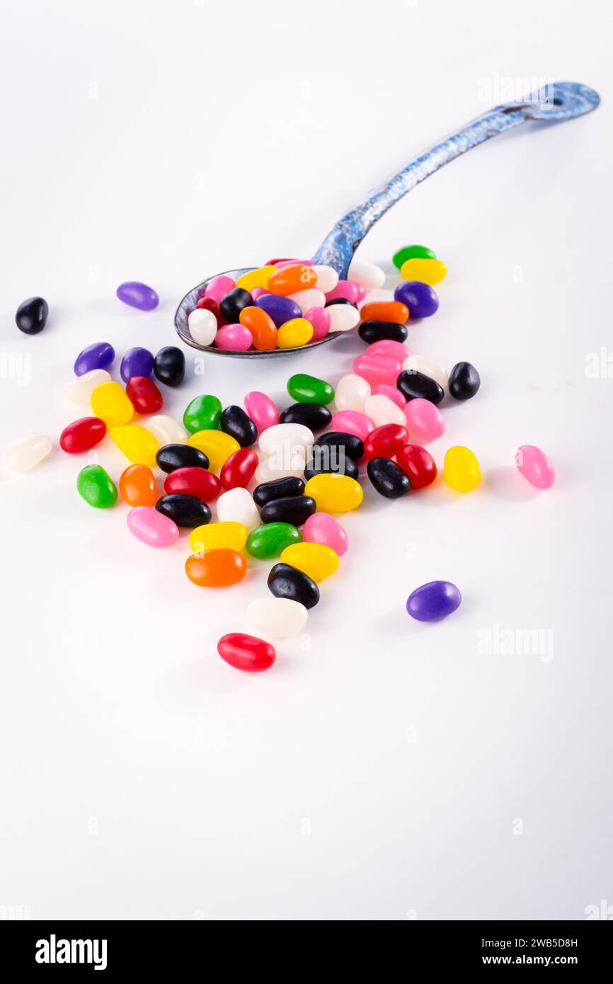 Natura morta verticale di gelatine colorate che fuoriescono da un grande cucchiaio su sfondo bianco Foto Stock