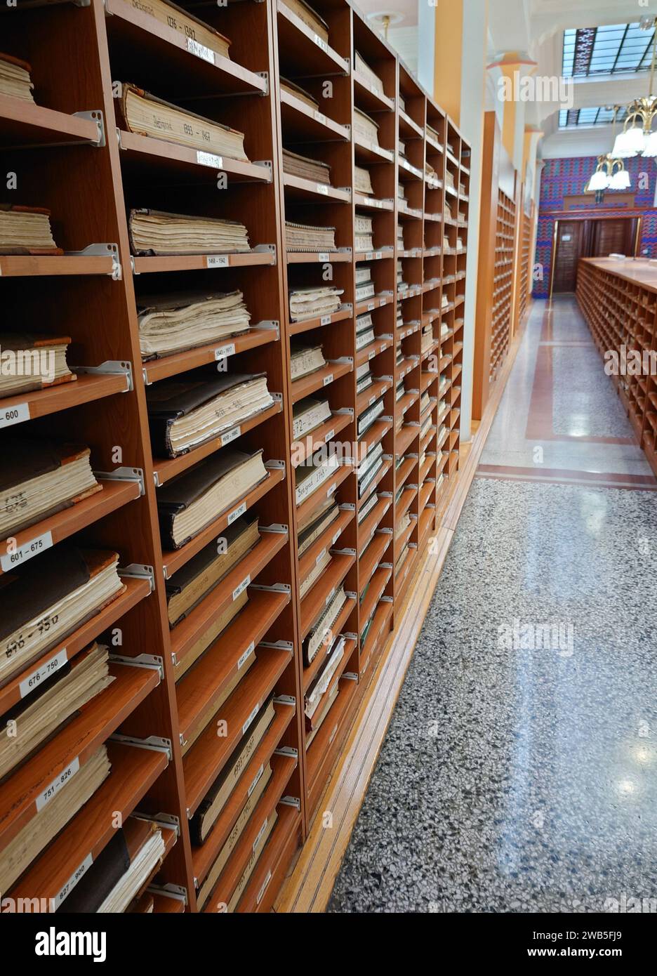 Vecchi scaffali in legno con documenti che rivestono l'ufficio catastale in un vecchio edificio secessionista con un pavimento in terrazzo lucido Foto Stock Vecchi scaffali in legno con documenti che rivestono l'ufficio catastale in un vecchio edificio secessionista con un pavimento in terrazzo lucido Foto Stock
