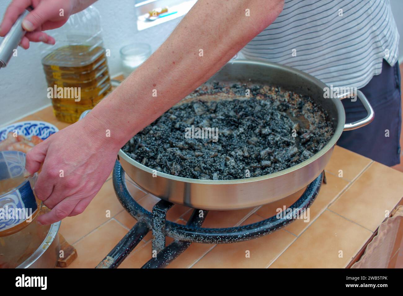 Osserva l'abilità artistica di un appassionato di cucina mentre mani esperte mescolano meticolosamente gli ingredienti, evocando un incantevole recipiente di riso nero fatto in casa. TH Foto Stock