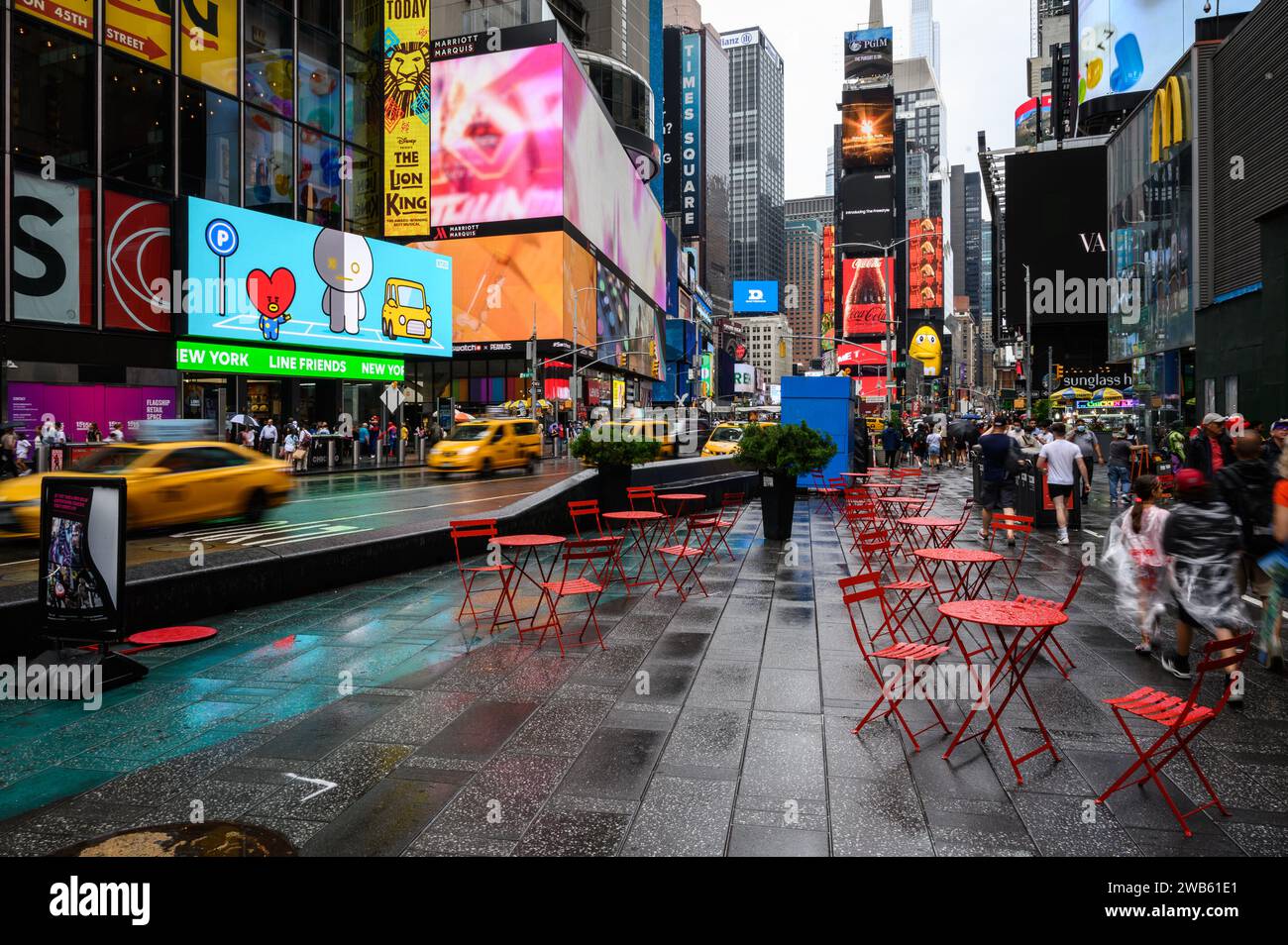 Times Square a New York, un pomeriggio piovoso. Sedie e tavoli metallici rossi vuoti. Passaggio dei taxi gialli. Foto Stock