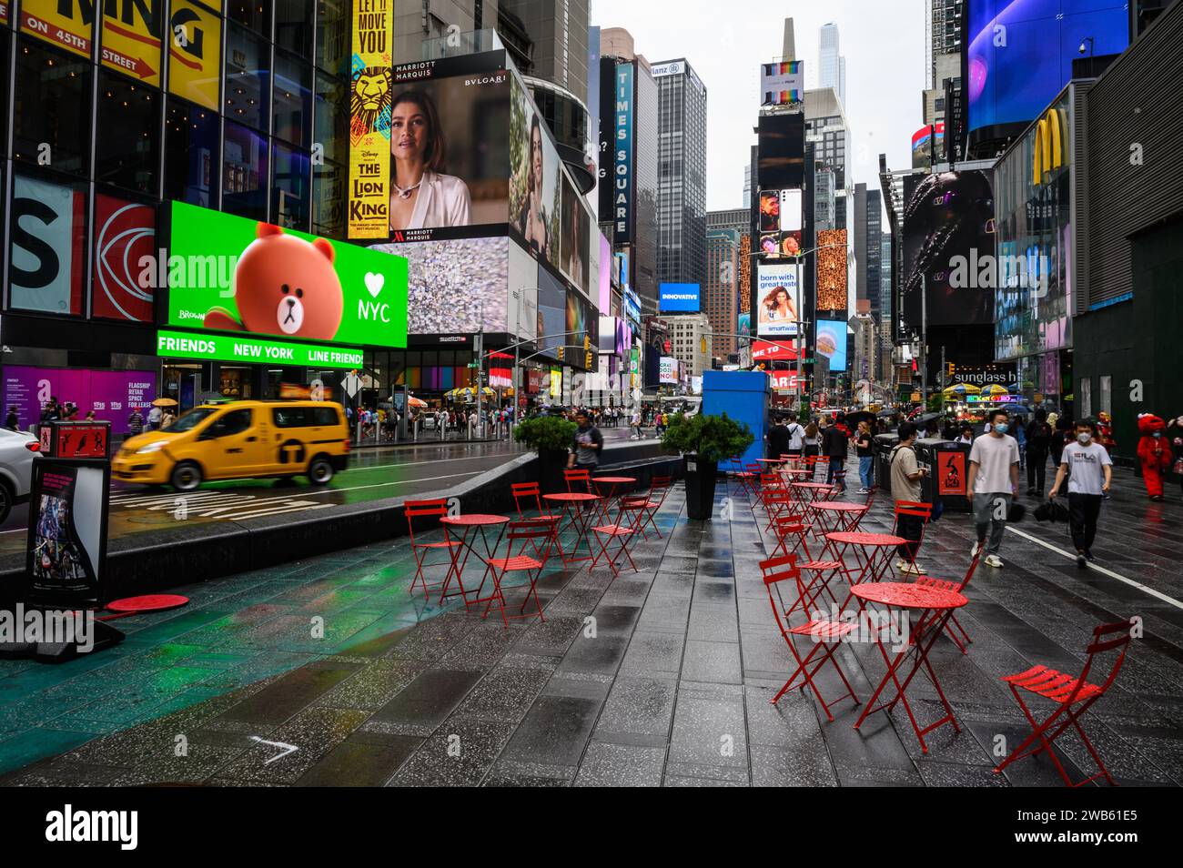 Times Square a New York, un pomeriggio piovoso. Sedie e tavoli metallici rossi vuoti. Passaggio dei taxi gialli. Foto Stock