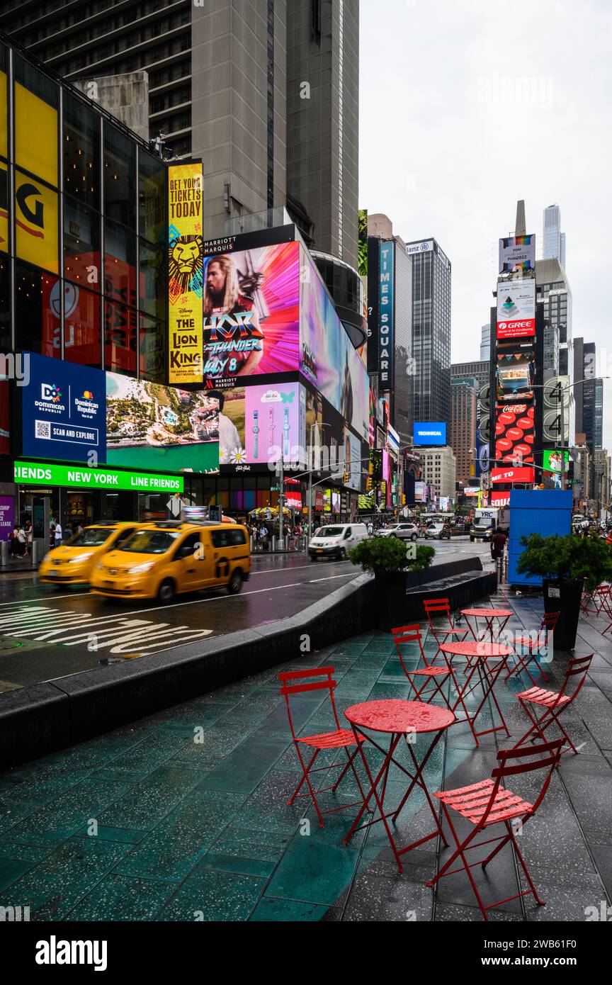 Times Square a New York, un pomeriggio piovoso. Sedie e tavoli metallici rossi vuoti. Passaggio dei taxi gialli. Foto Stock