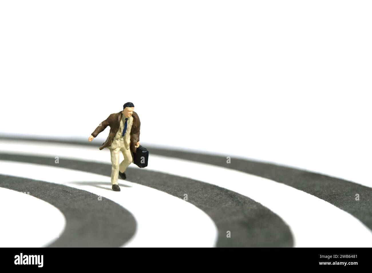 Fotografia di figure giocattolo in miniatura. Un uomo d'affari che corre sopra la linea di binari che trasporta una valigetta. Isolato su sfondo bianco. Immagine Foto Stock