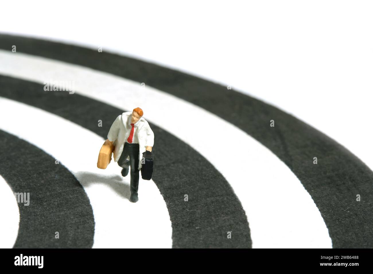 Fotografia di figure giocattolo in miniatura. Un uomo d'affari che corre sopra la linea di binari che trasporta una valigetta. Isolato su sfondo bianco. Immagine Foto Stock