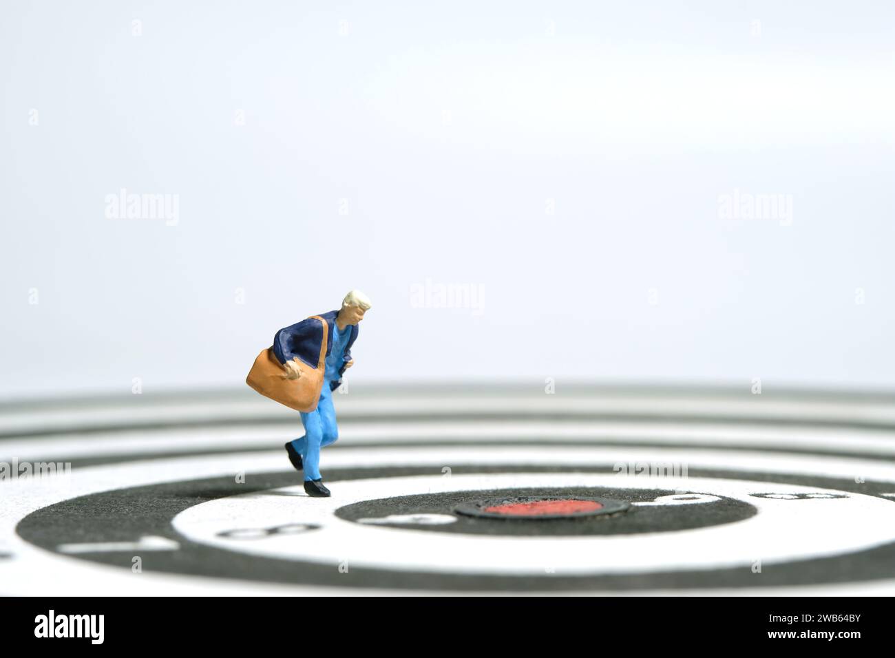 Fotografia di figure giocattolo in miniatura. Una studentessa universitaria che corre su una borsa per il trasporto di freccette. Isolato su sfondo bianco. Foto immagine Foto Stock