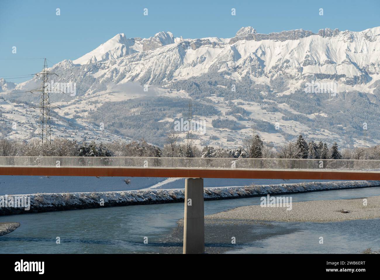 Vaduz, Liechtenstein, 3 dicembre 2023 atmosfera invernale al fiume reno con un ponte pedonale e splendide alpi bianche sullo sfondo Foto Stock