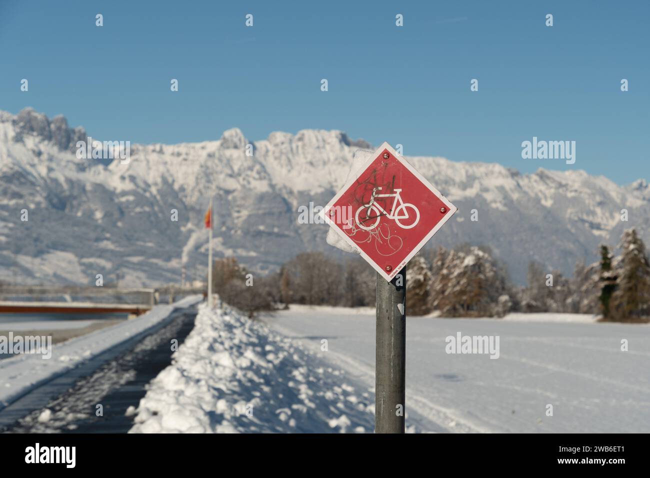 Vaduz, Liechtenstein, 3 dicembre 2023 simbolo della bicicletta presso la diga del fiume reno in un fantastico paesaggio invernale e montagne bianche sullo sfondo Foto Stock