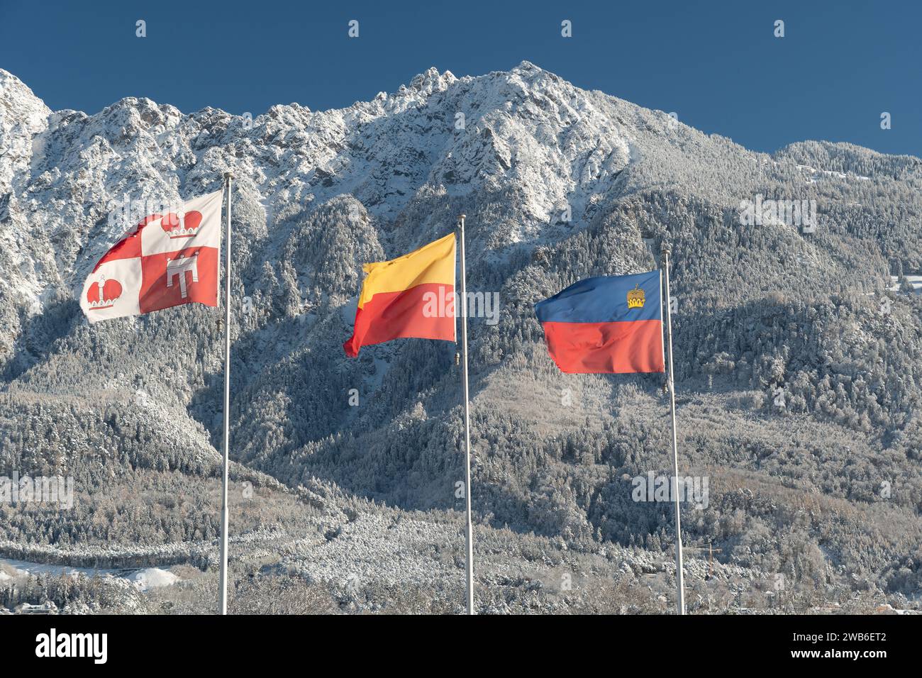 Vaduz, Liechtenstein, 3 dicembre 2023, la bandiera nazionale sventola nel vento di fronte alle impressionanti alpi innevate in una giornata di sole Foto Stock