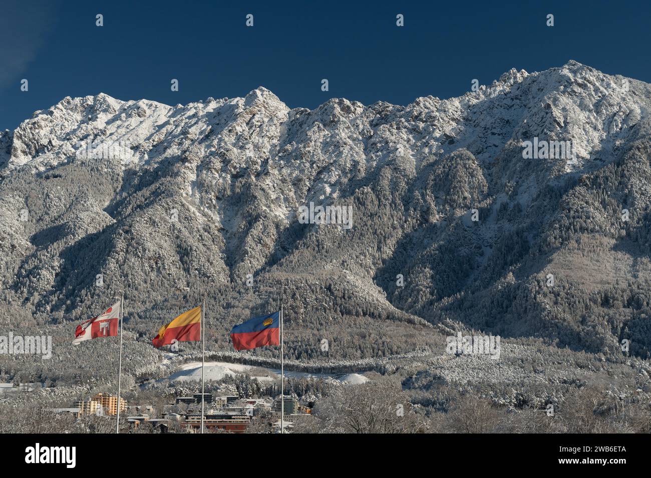 Vaduz, Liechtenstein, 3 dicembre 2023, la bandiera nazionale sventola nel vento di fronte alle impressionanti alpi innevate in una giornata di sole Foto Stock