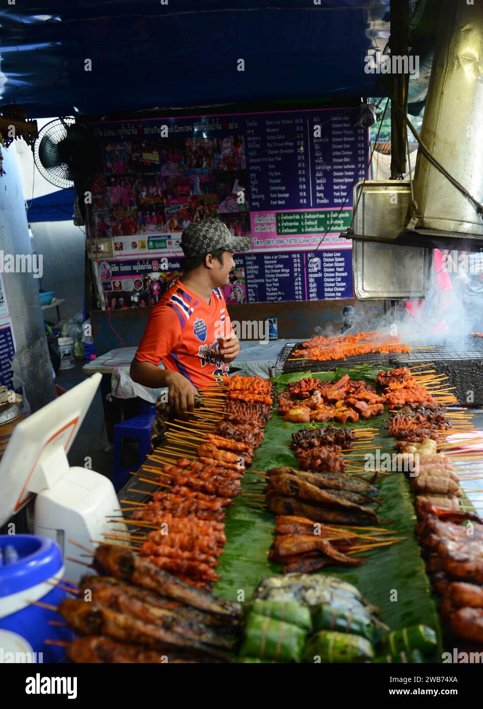 Un uomo tailandese che grigia pollo in un piccolo Street food su Soi Naradhiwas Rajanagarindra a Bangkok, Thailandia. Foto Stock