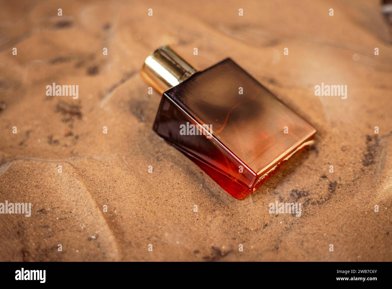 Una bottiglia di profumo di lusso color arancio scuro dorato conservata nella sabbia bagnata. Foto Stock
