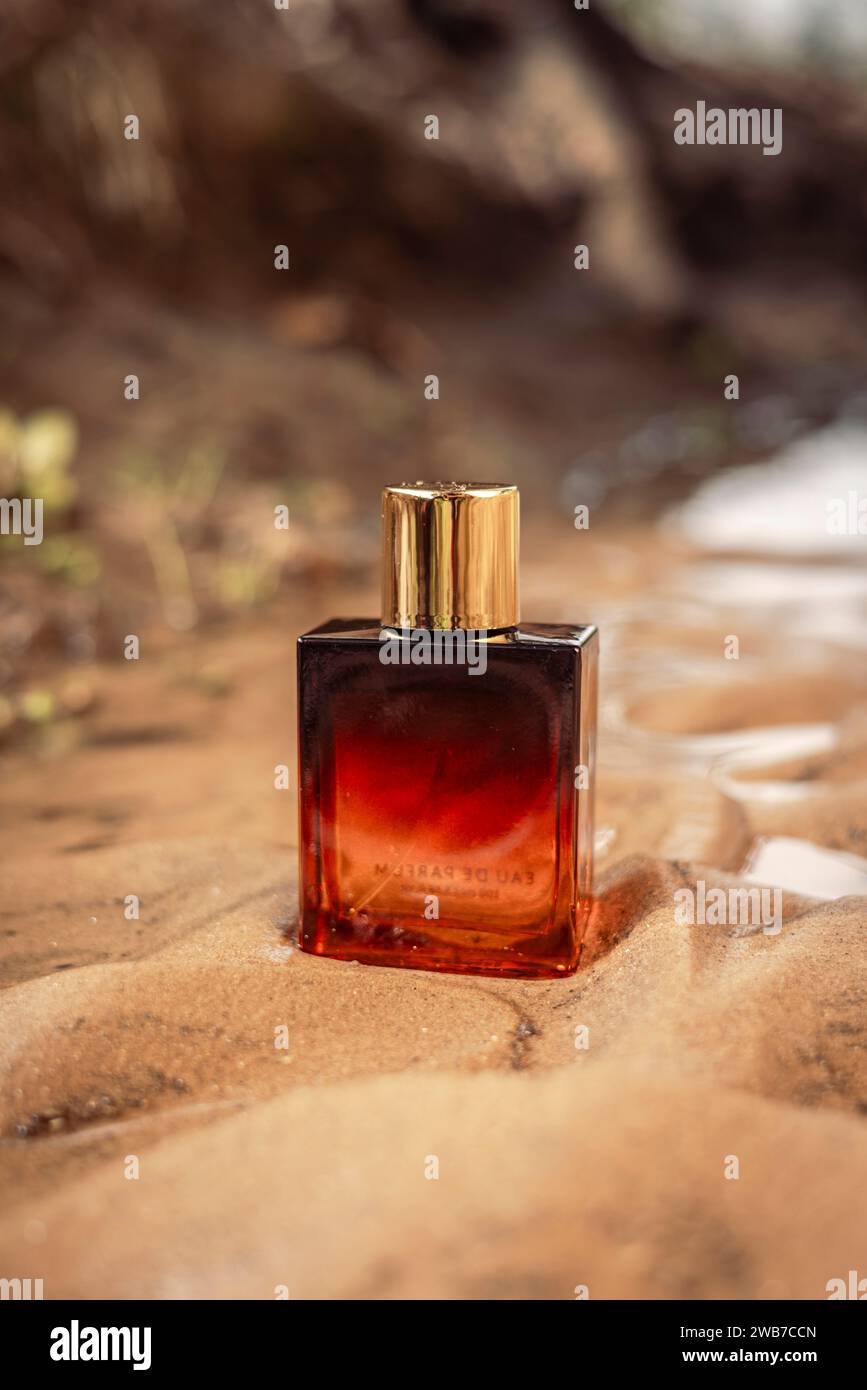 Una bottiglia di profumo di lusso color arancio scuro dorato conservata nella sabbia bagnata. Foto Stock