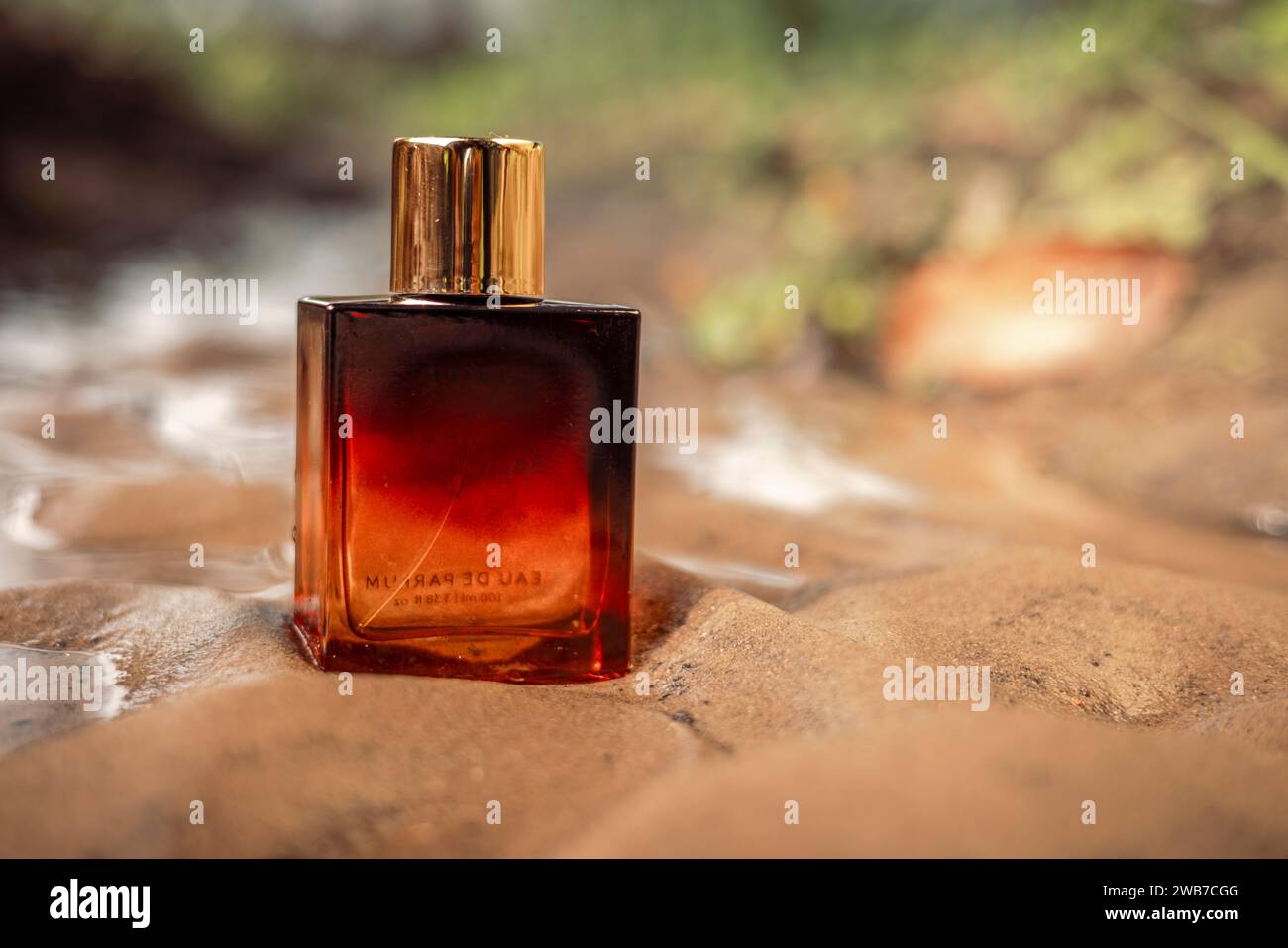 Una bottiglia di profumo di lusso color arancio scuro dorato conservata nella sabbia bagnata. Foto Stock