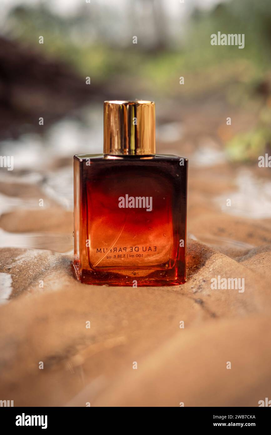 Una bottiglia di profumo di lusso color arancio scuro dorato conservata nella sabbia bagnata. Foto Stock