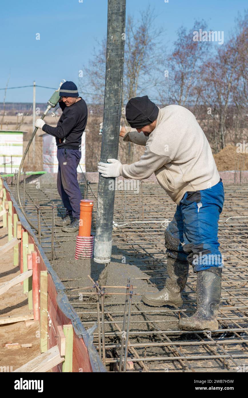 REGIONE DI LENINGRADO, RUSSIA - 28 MARZO 2021: I lavoratori migranti versano cemento sulla fondazione di una casa di campagna in una soleggiata giornata di marzo Foto Stock
