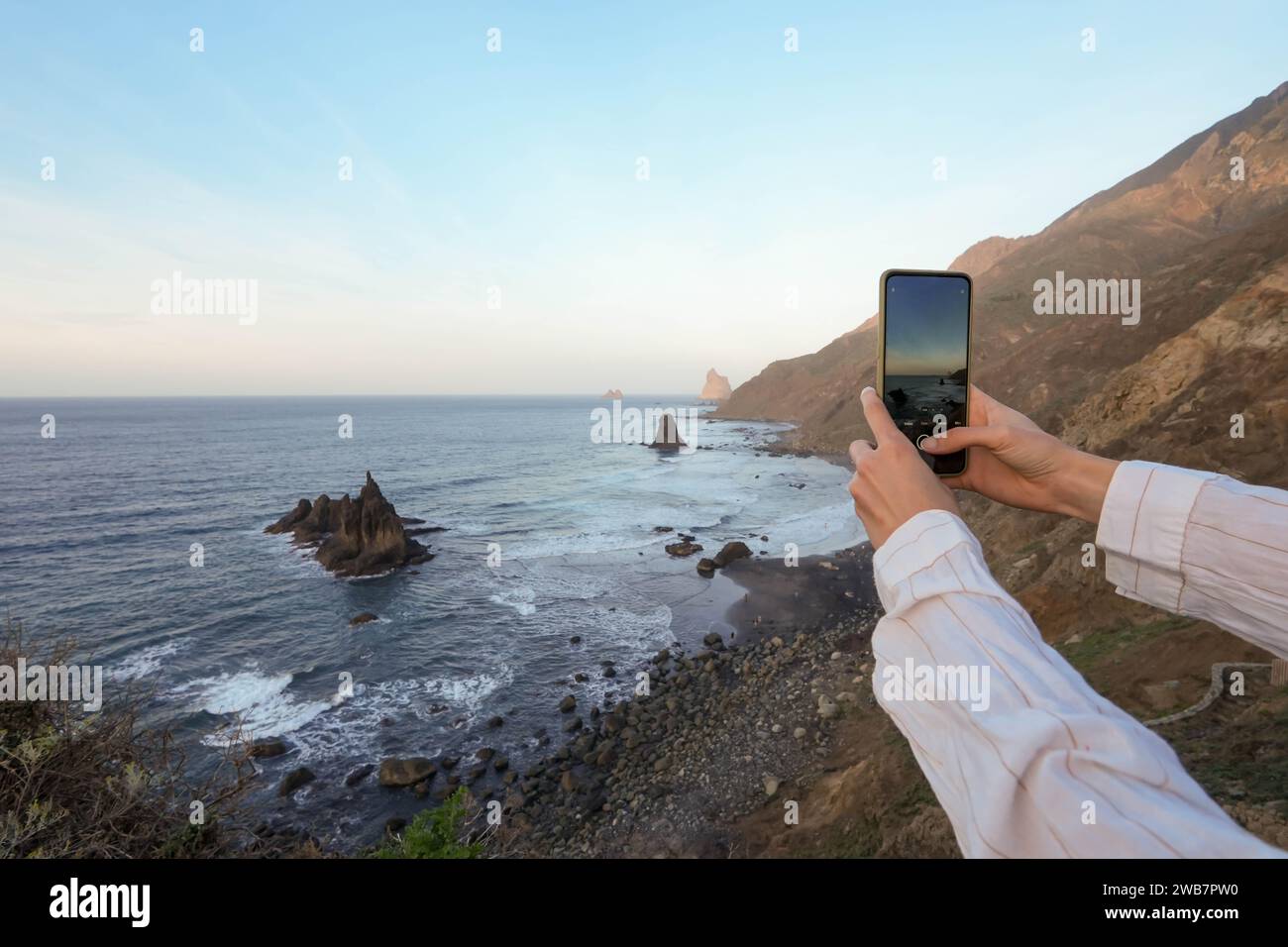 Giovane donna che cattura la tranquilla bellezza di Benijo Beach, Tenerife, con il suo caratteristico litorale roccioso e le calme acque azzurre, durante l'Ou dorato Foto Stock