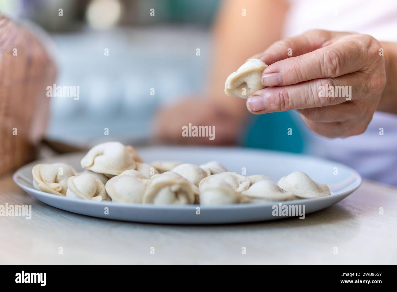 scolpire i gnocchi a mano con le mani nella farina. un'anziana donna tiene in mano gnocchi modellati. Foto Stock