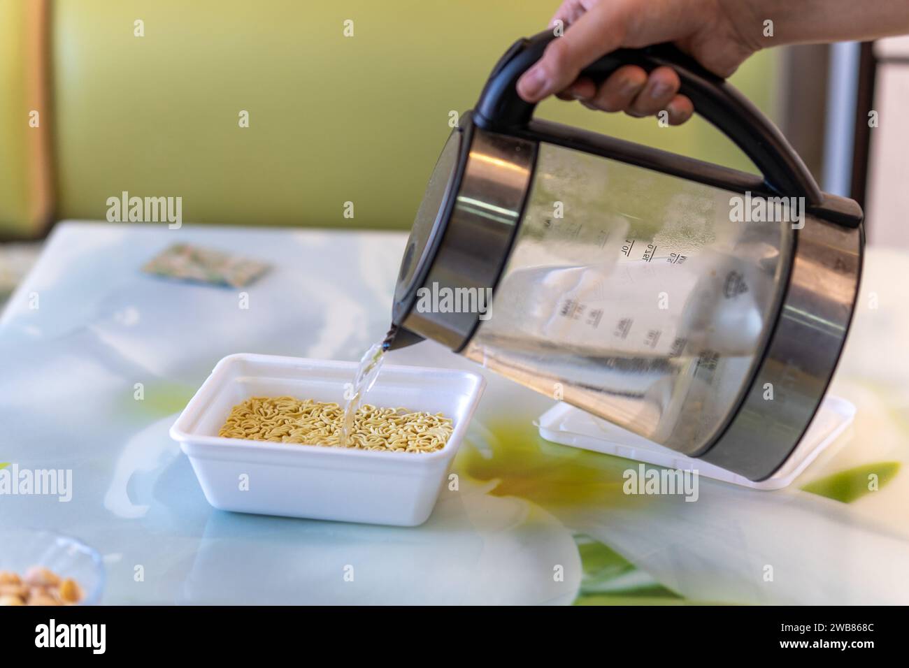 L'acqua bollente del bollitore viene riempita con spaghetti istantanei in una scatola. Cibo veloce e soddisfacente. Foto Stock